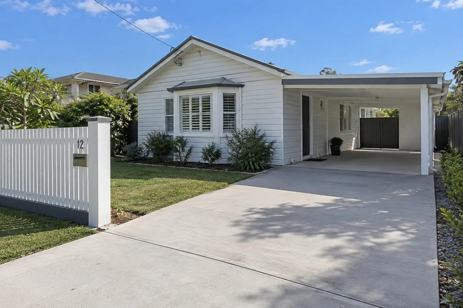 Newly installed concrete driveway running past a white weatherboard Mackay home to its carport