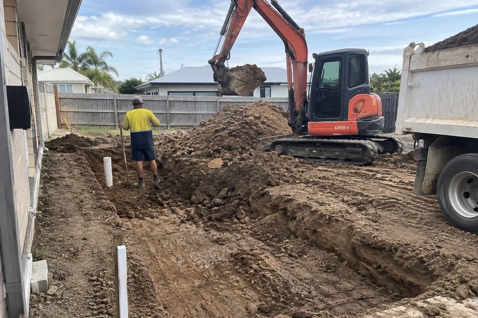 Excavator digging beside a Mackay home and loading spoil into a tipper truck